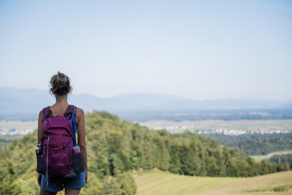 Eine Person mit Rucksack steht auf einer Anhöhe und blickt über eine weite Landschaft
